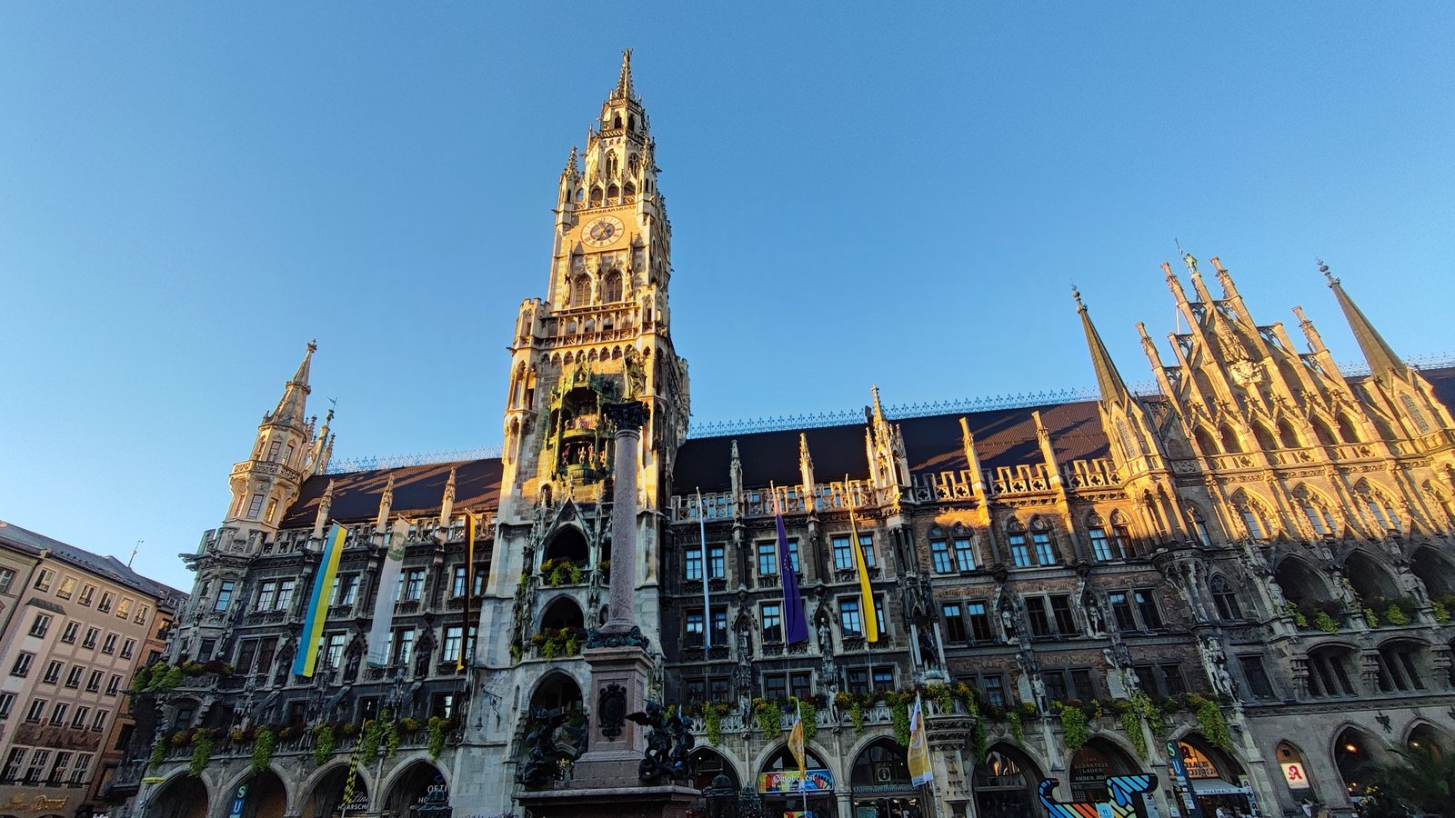 The Neues Rathaus on Marienplatz in Munich, its clock tower and Gothic spires lit gold by the evening sun against a clear blue sky